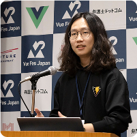 Vue Fes Japan 2024で登壇するAnthony。Vue Fes Japan のロゴ とスポンサーのロゴが並ぶバックパネルの前で、マイク越しに発表している。