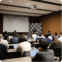 Vue Fes Japan 2024のセッション中、スクリーンを見ながら登壇者の発表を聞いている参加者たち。会場はノートパソコンを広げた人々で賑わっている。