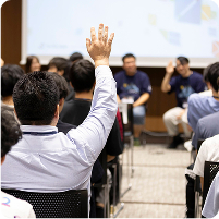 Vue Fes Japan 2024のセッション中、観客席から手を挙げて質問する参加者。前方にはスピーカーが座っている。